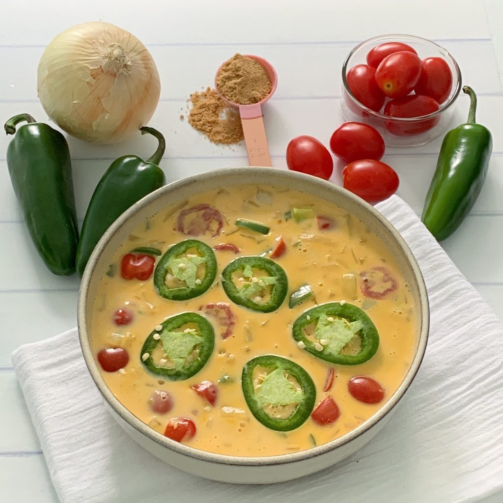 An Authentic Easy Queso Dip Recipe featured by top US food blog, Food Diary of a City Girl: image of a bowl with queso dip surrounded by onion, three peppers, and cherry tomatoes.