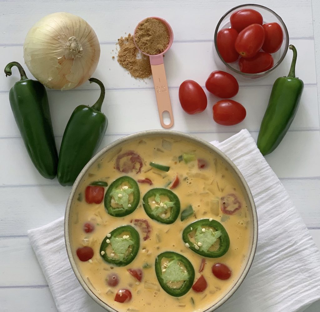 An Authentic Easy Queso Dip Recipe featured by top US food blog, Food Diary of a City Girl: image of a bowl with queso dip surrounded by onion, three peppers, and cherry tomatoes.