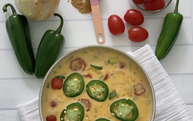 An Authentic Easy Queso Dip Recipe featured by top US food blog, Food Diary of a City Girl: image of a bowl with queso dip surrounded by onion, three peppers, and cherry tomatoes.