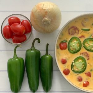 An Authentic Easy Queso Dip Recipe featured by top US food blog, Food Diary of a City Girl: image of a bowl with queso dip surrounded by onion, three peppers, and cherry tomatoes.