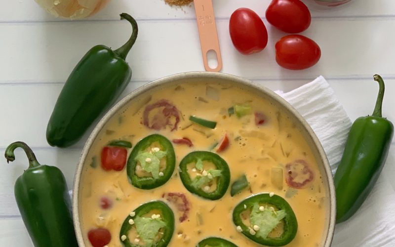 An Authentic Easy Queso Dip Recipe featured by top US food blog, Food Diary of a City Girl: image of a bowl with queso dip surrounded by onion, three peppers, and cherry tomatoes.