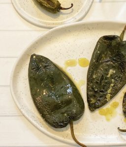 How to Roast Chili Peppers in the Oven: 5 Easy Steps featured by top US food blog, Food Diary of a City Girl: image of two roasted poblano peppers on a speckled pottery plate.