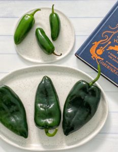 How to Roast Chili Peppers in the Oven: 5 Easy Steps featured by top US food blog, Food Diary of a City Girl: image of three fresh poblano peppers on a speckled pottery plate, three fresh jalapeño peppers on a small speckled pottery plate, and a blue book.